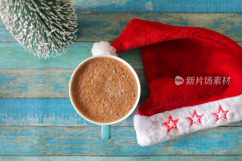 一组物体的图像，包括圣诞树模型，蓝色杯热巧克力饮料/热可可和红白圣诞帽的蓝色背景，蓝绿色的舌头和槽效果的背景，圣诞概念，高架视野